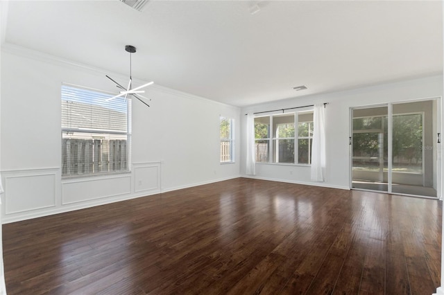 unfurnished living room with crown molding, plenty of natural light, dark hardwood / wood-style floors, and an inviting chandelier