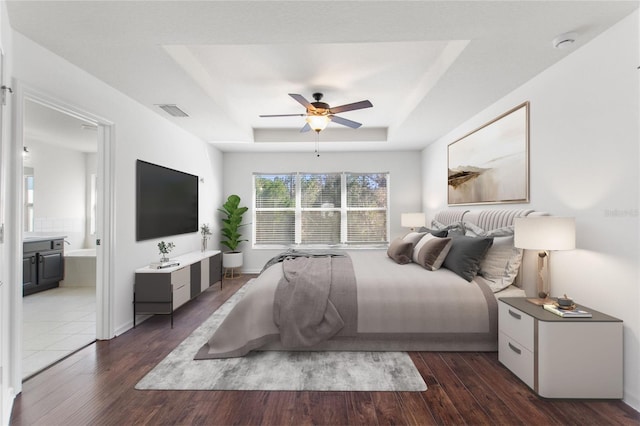 bedroom with a tray ceiling, ceiling fan, dark hardwood / wood-style flooring, and ensuite bathroom