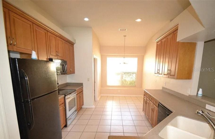 kitchen with sink, light tile patterned flooring, hanging light fixtures, and appliances with stainless steel finishes