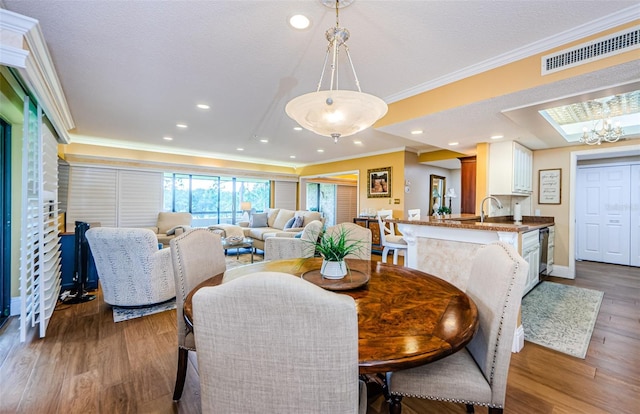 dining space featuring a textured ceiling, wood-type flooring, crown molding, and a chandelier