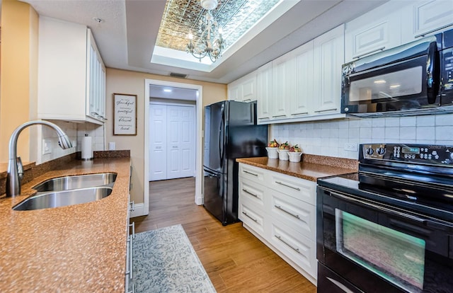 kitchen featuring black appliances, white cabinets, sink, a skylight, and light hardwood / wood-style floors