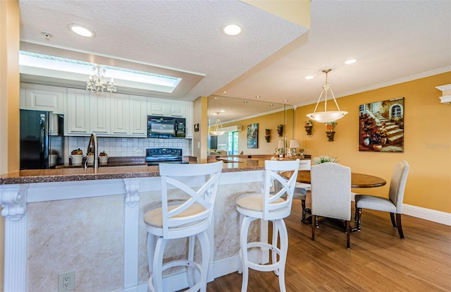 kitchen with white cabinetry, hanging light fixtures, a kitchen breakfast bar, tasteful backsplash, and black appliances