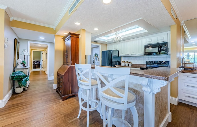 kitchen with black appliances, white cabinets, a skylight, a textured ceiling, and a kitchen island