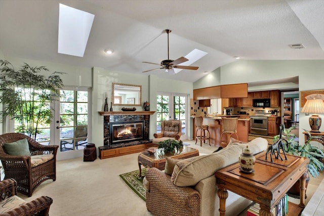 living room with french doors, light carpet, ceiling fan, a premium fireplace, and vaulted ceiling with skylight