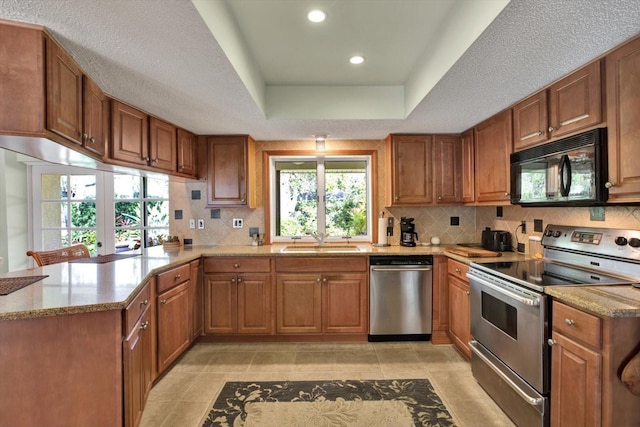 kitchen with appliances with stainless steel finishes, kitchen peninsula, light stone counters, a tray ceiling, and sink