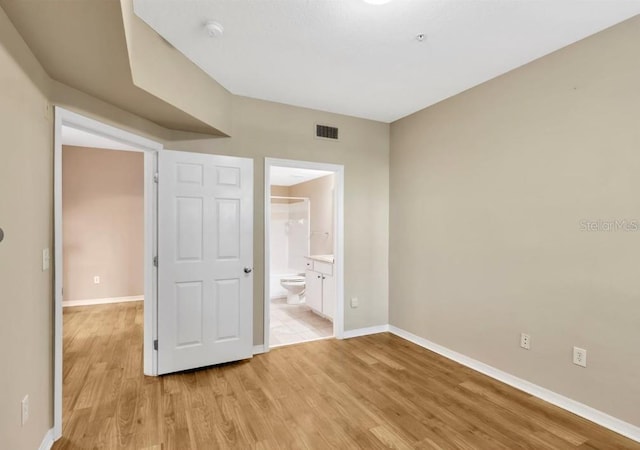 unfurnished bedroom with light wood-type flooring and connected bathroom