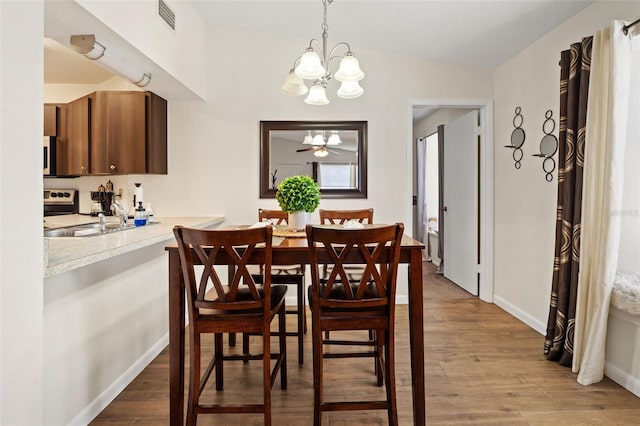 dining space with hardwood / wood-style floors, an inviting chandelier, lofted ceiling, and sink