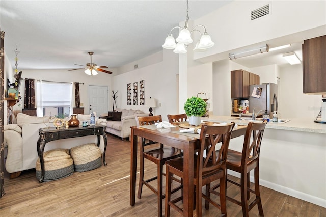 dining space with ceiling fan with notable chandelier and light wood-type flooring