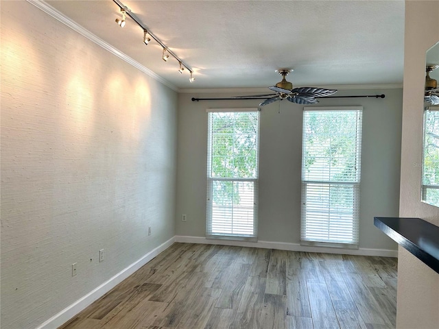 unfurnished room featuring plenty of natural light, ornamental molding, rail lighting, and wood-type flooring