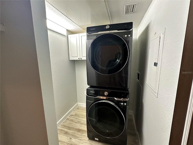 washroom featuring electric panel, light wood-type flooring, stacked washer and clothes dryer, a textured ceiling, and cabinets