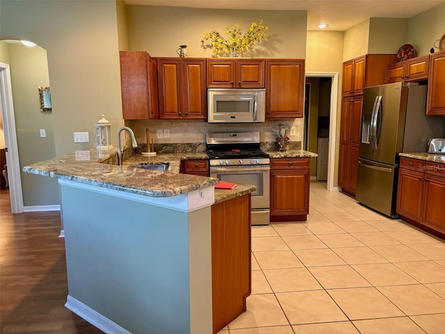 kitchen with appliances with stainless steel finishes, stone counters, sink, and kitchen peninsula