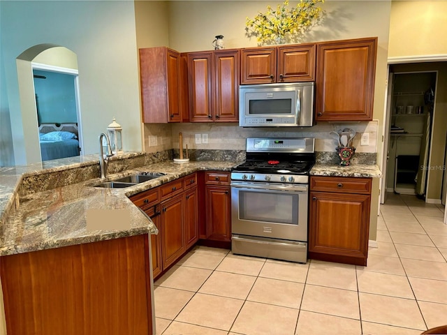 kitchen with appliances with stainless steel finishes, stone counters, kitchen peninsula, sink, and light tile patterned flooring