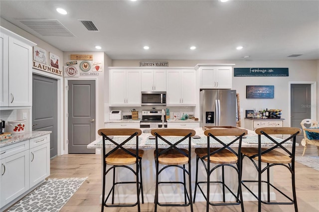 kitchen with light stone counters, white cabinets, a center island with sink, and appliances with stainless steel finishes