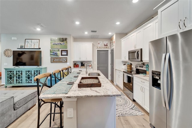 kitchen featuring a kitchen island with sink, a breakfast bar area, stainless steel appliances, light stone countertops, and sink