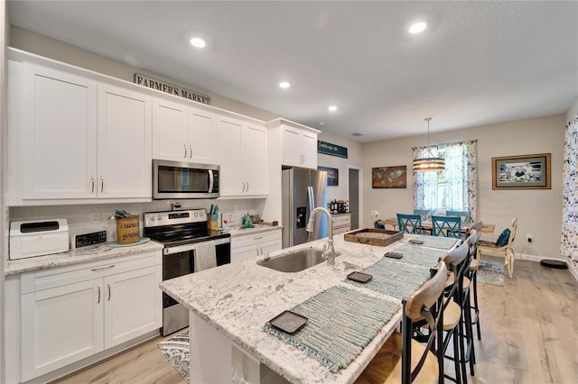 kitchen featuring a center island with sink, stainless steel appliances, pendant lighting, light stone counters, and sink