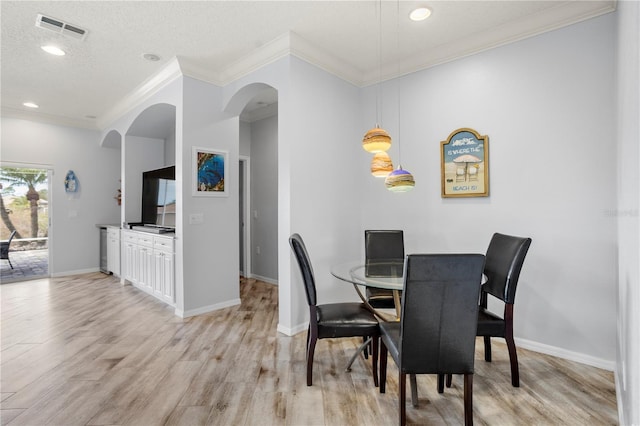 dining area with a textured ceiling, crown molding, and light wood-type flooring