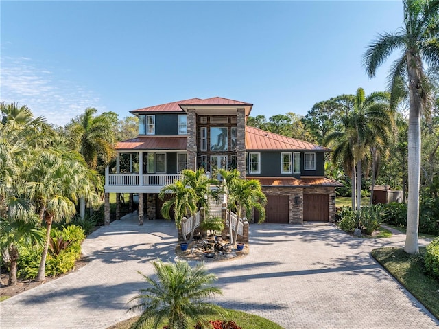 beach home featuring metal roof, an attached garage, stone siding, decorative driveway, and a standing seam roof