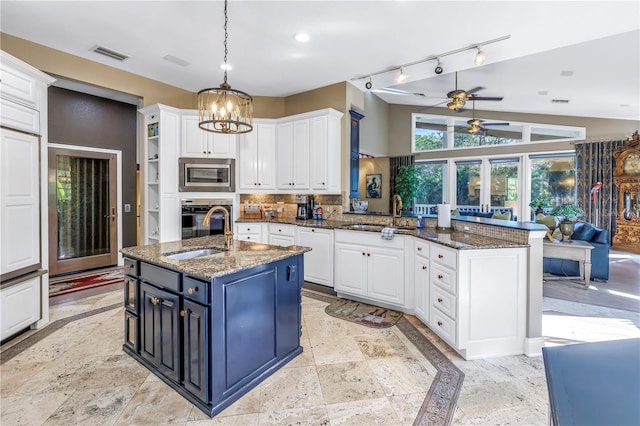 kitchen with oven, stainless steel microwave, sink, white cabinets, and a center island with sink