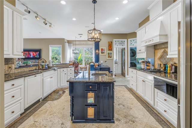 kitchen with kitchen peninsula, sink, backsplash, a kitchen island with sink, and dark stone countertops