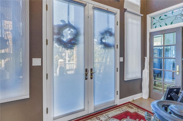 entryway with french doors, a textured wall, and baseboards