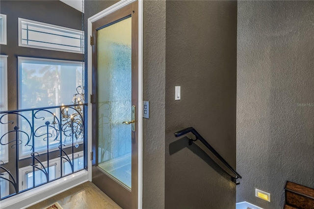 doorway to outside with vaulted ceiling, wood finished floors, and a textured wall