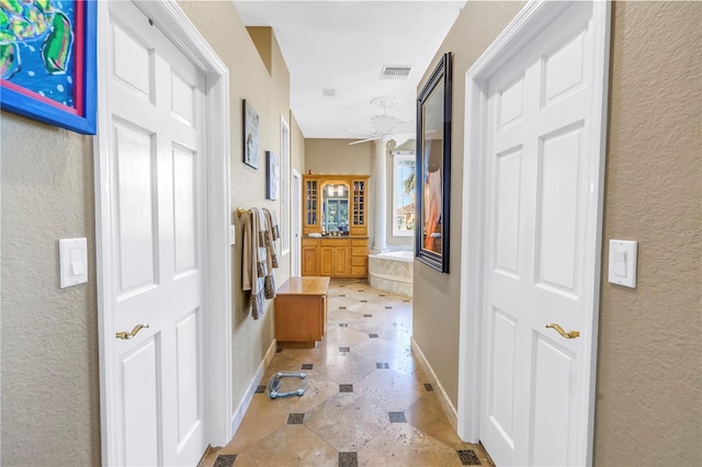 hall featuring visible vents, a textured wall, and baseboards