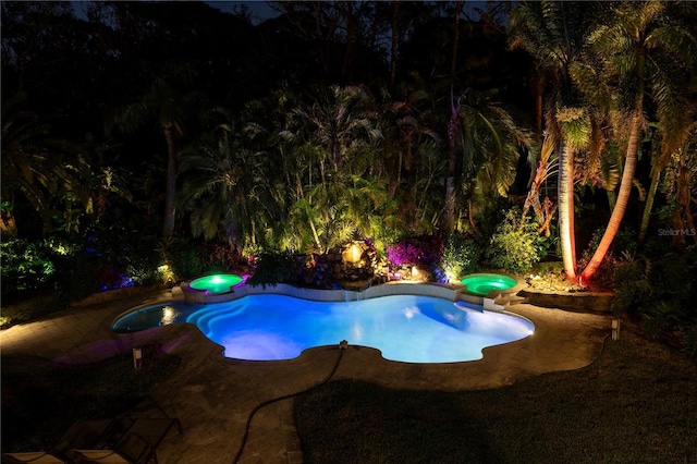 pool at twilight featuring a patio and a pool with connected hot tub