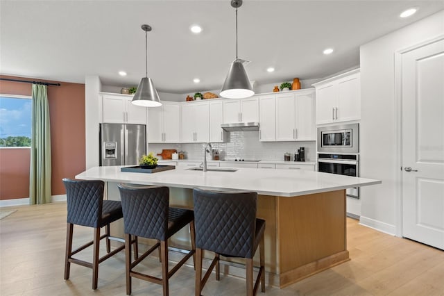 kitchen featuring decorative light fixtures, stainless steel appliances, decorative backsplash, a kitchen island with sink, and white cabinets