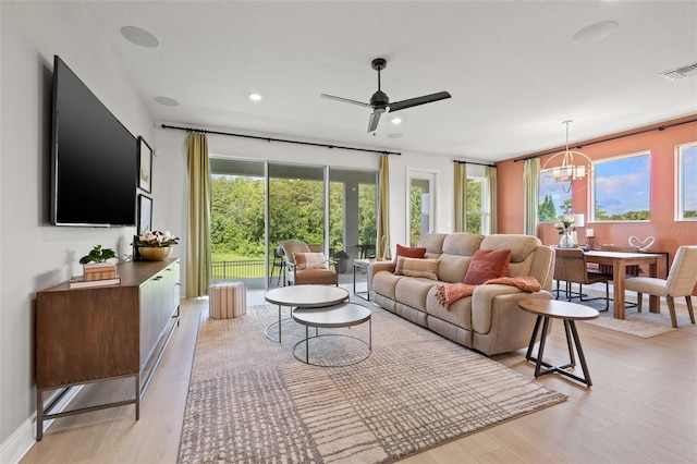 living room with ceiling fan with notable chandelier and light hardwood / wood-style floors