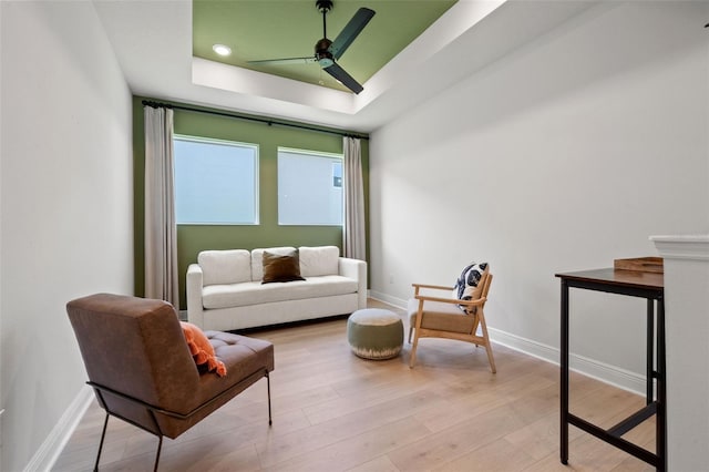 sitting room with light wood-type flooring, ceiling fan, and a tray ceiling