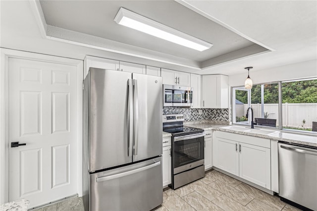 kitchen with stainless steel appliances, sink, white cabinetry, backsplash, and a tray ceiling