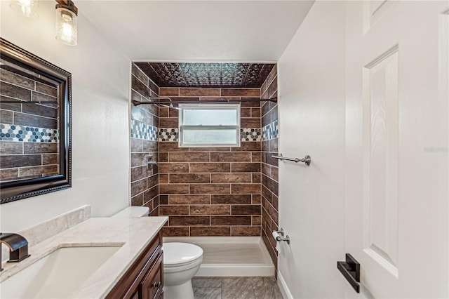 bathroom with toilet, a tile shower, and vanity