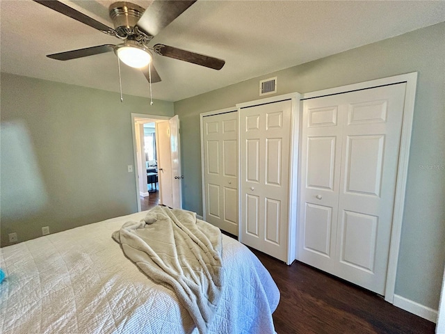 bedroom featuring ceiling fan, dark hardwood / wood-style floors, and two closets