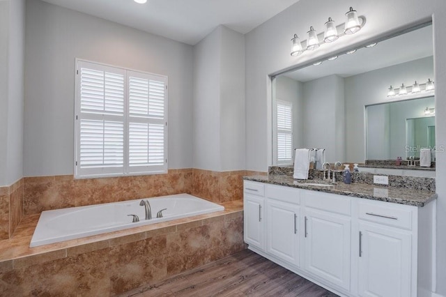 bathroom with tiled bath, wood-type flooring, and vanity