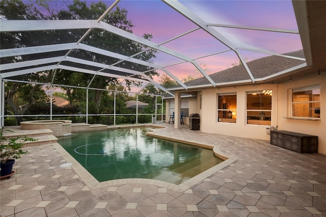 pool at dusk featuring glass enclosure, a patio area, and an in ground hot tub