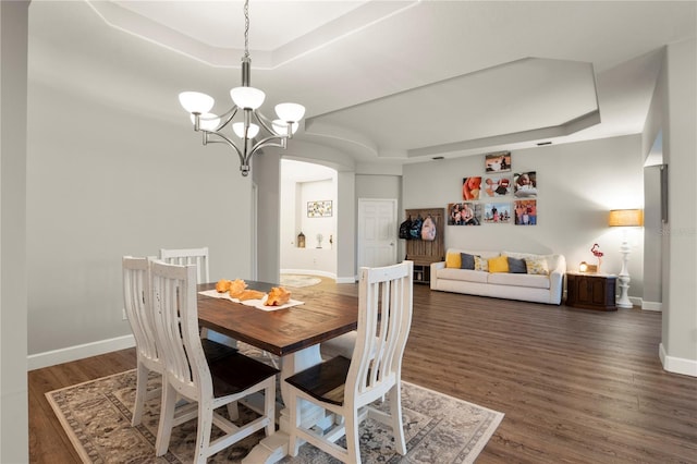 dining space featuring a raised ceiling, dark hardwood / wood-style flooring, and a chandelier