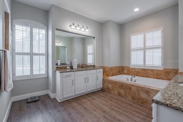 bathroom featuring a wealth of natural light, a relaxing tiled tub, hardwood / wood-style floors, and vanity