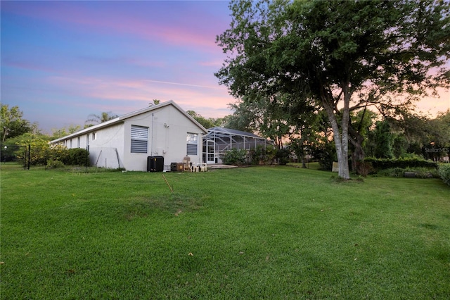 yard at dusk featuring glass enclosure and cooling unit