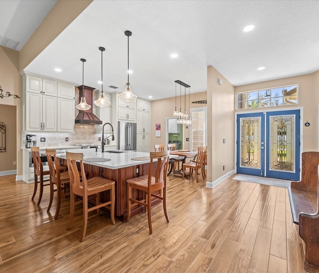 kitchen featuring white cabinetry, sink, a large island with sink, light hardwood / wood-style floors, and decorative light fixtures