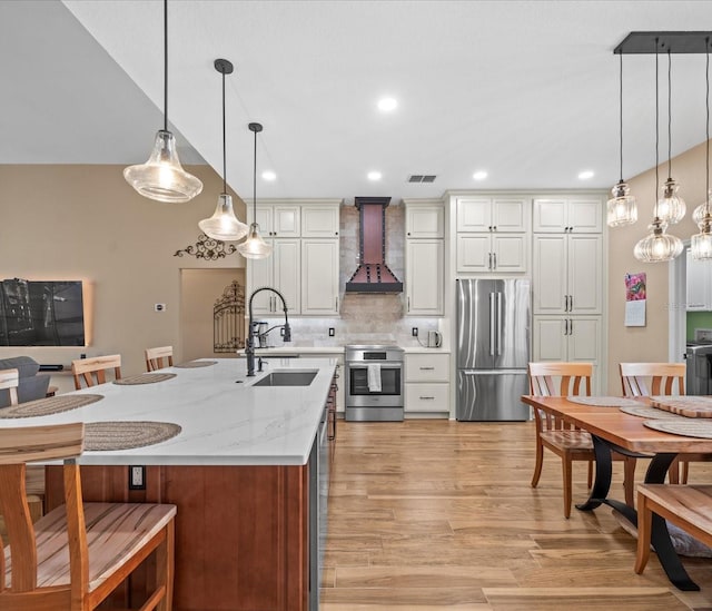 kitchen with light stone countertops, sink, hanging light fixtures, custom range hood, and appliances with stainless steel finishes