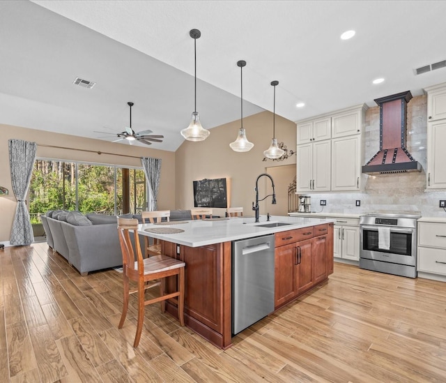 kitchen with white cabinets, wall chimney range hood, a kitchen island with sink, and appliances with stainless steel finishes