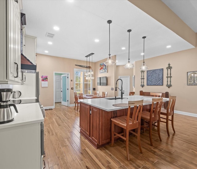 kitchen featuring pendant lighting, sink, an island with sink, and light hardwood / wood-style flooring