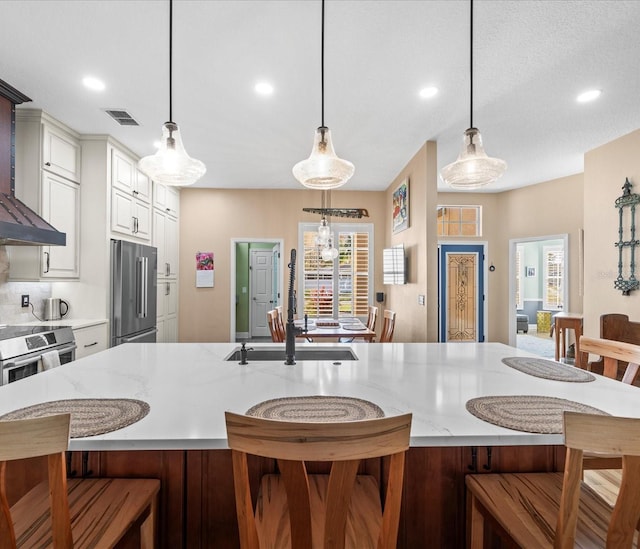 kitchen featuring a spacious island, hanging light fixtures, light stone countertops, white cabinetry, and stainless steel appliances