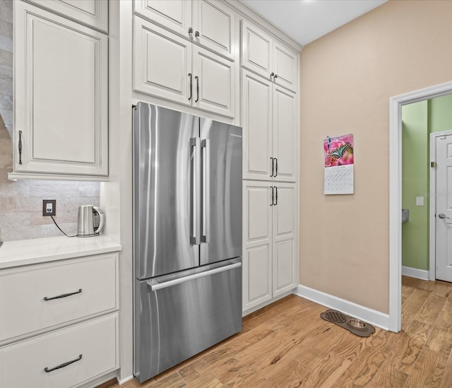 kitchen with backsplash, stainless steel fridge, light hardwood / wood-style flooring, and white cabinets