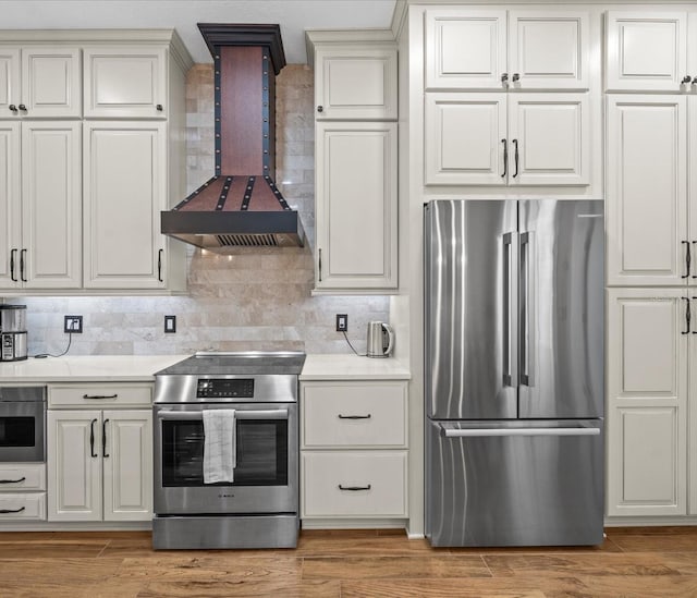 kitchen featuring custom exhaust hood, decorative backsplash, wood-type flooring, and appliances with stainless steel finishes