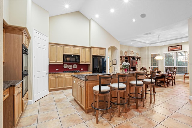 kitchen with light tile patterned floors, high vaulted ceiling, a breakfast bar area, black appliances, and an island with sink