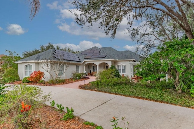 view of front of home featuring roof mounted solar panels, driveway, and stucco siding