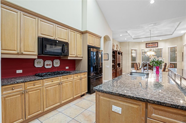 kitchen with light tile patterned floors, dark stone countertops, arched walkways, black appliances, and a sink