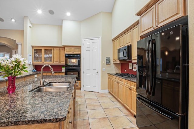 kitchen featuring light tile patterned flooring, dark stone countertops, black appliances, and a sink