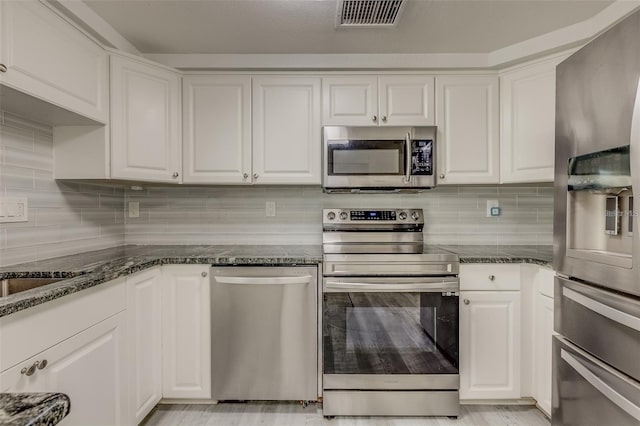 kitchen featuring appliances with stainless steel finishes, white cabinetry, and dark stone counters